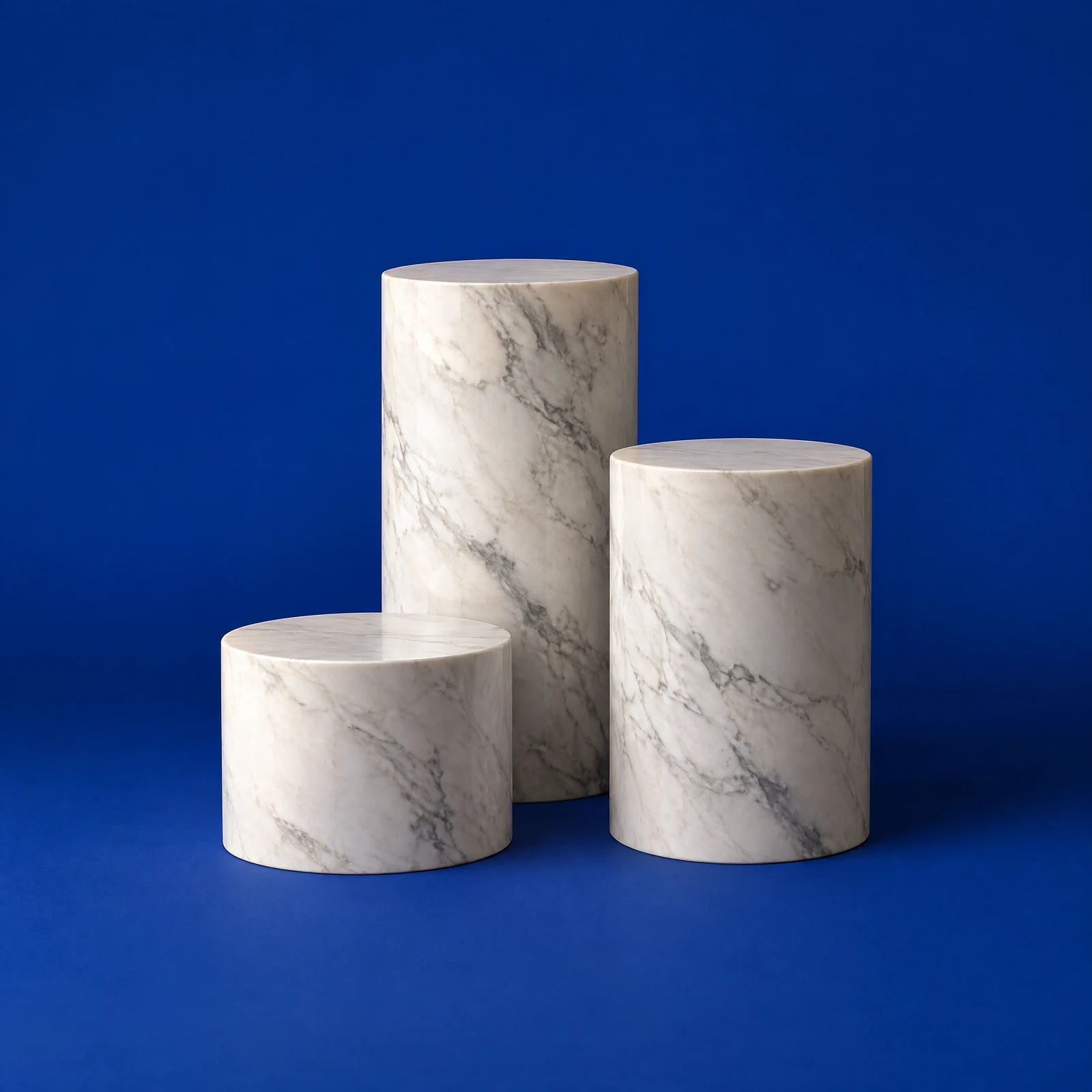 White veined marble cylinder podiums of different heights standing together on a cobalt blue background